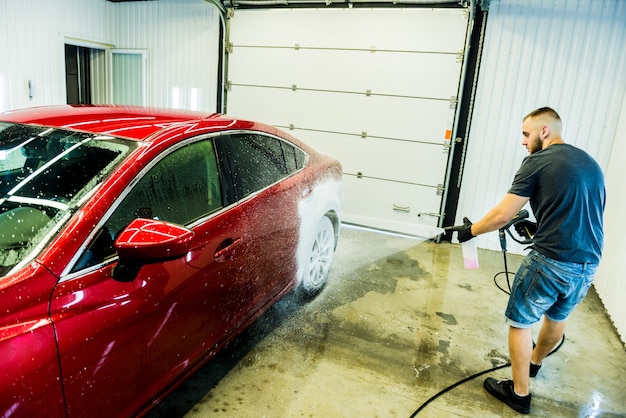 Arbeiter, der Auto mit aktivem Schaum auf einer Autowäsche wäscht.