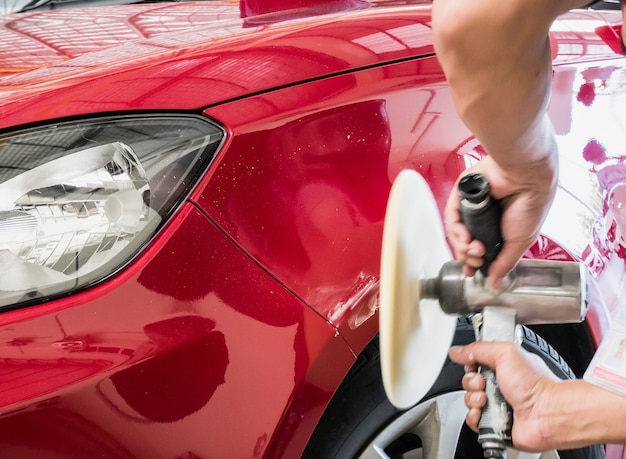 Arbeiter, der das Auto mit Polieren und Wachsen des roten Autos reinigt