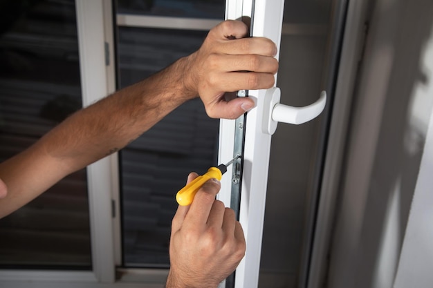 Arbeiter, der das Fenster mit einem Schraubendreher befestigt, der ein neues Kunststofffenster im Haus installiert