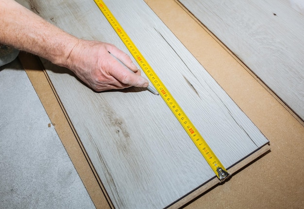 Arbeiter, der Laminatböden in der Wohnung herstellt Maßband und Bleistift in den Händen Wartung Reparatur Renovierung Parkettbohlen aus Holz im Innenbereich