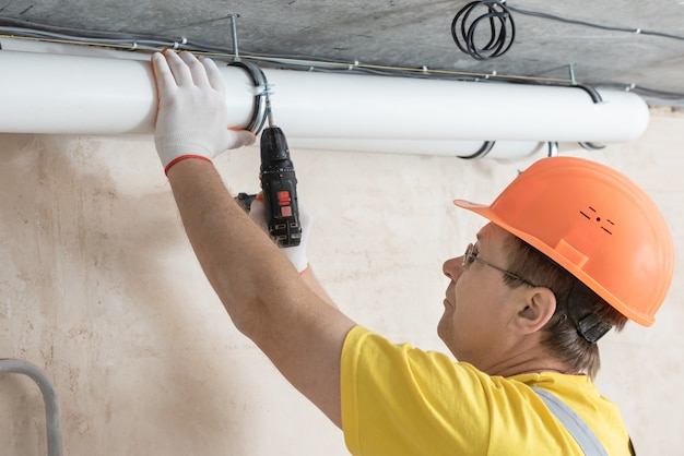 Arbeiter, der mit einem Schraubendreher Lüftungsrohre an der Decke befestigt