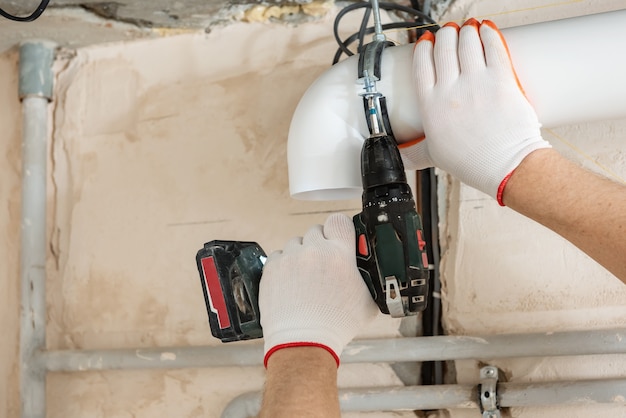 Arbeiter, der mit einem Schraubendreher Lüftungsrohre an der Decke befestigt