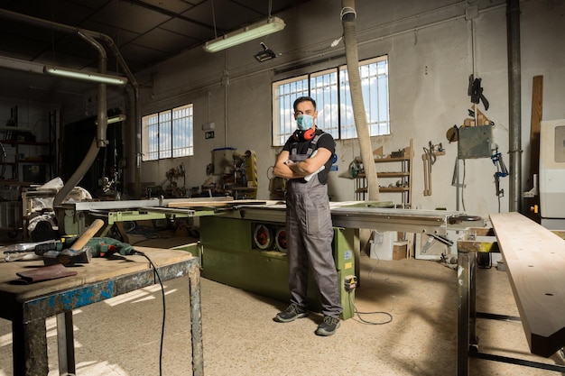 Arbeiter, die in einer Fabrik mit Maske und Schutzausrüstung stehen und die Kamera betrachten. Totaler Schuss, voller Körper.