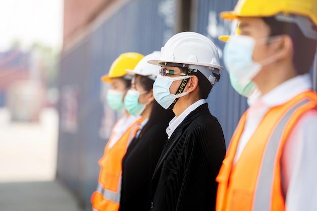 Arbeiter, die Schutzmaskengesicht und Sicherheitsausrüstung neben Frachtcontainern tragen