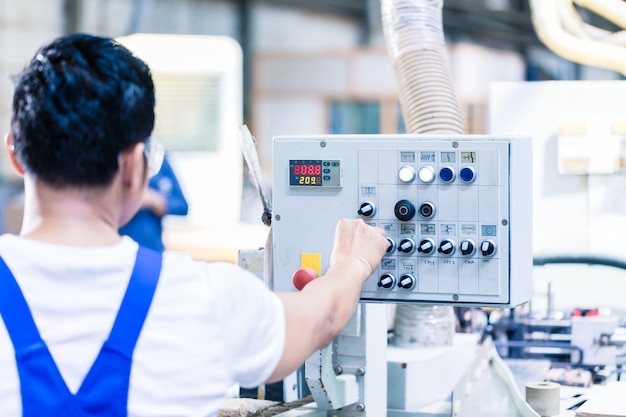 Arbeiter drückt Knöpfe auf der CNC-Maschinensteuerkarte in der asiatischen Fabrik