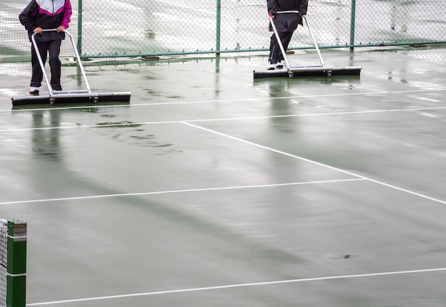 Arbeiter entfernen Wasser vom Tennisplatz.