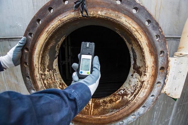 Arbeiter Hand hält Gasdetektor Inspektion Sicherheitsgasprüfung am Edelstahltank des vorderen Mannlochs