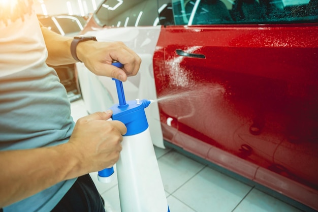 Arbeiter im Autoservice sprüht Wasser auf das Auto, bevor er eine Schutzfolie aufträgt