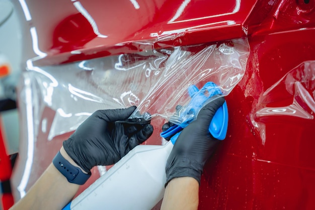 Arbeiter im Autoservice sprüht Wasser auf das Auto, bevor er eine Schutzfolie aufträgt