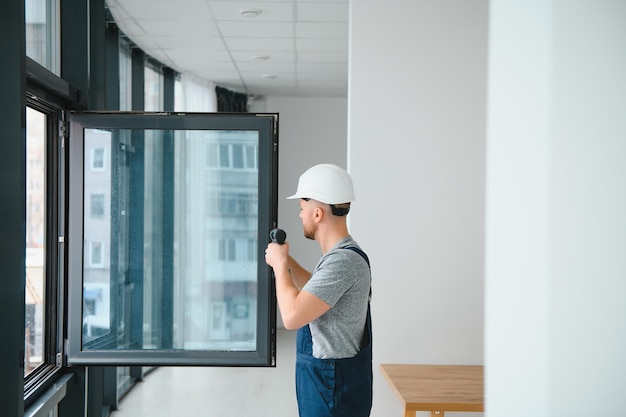 Arbeiter im Overall, der Kunststofffenster im Wohnzimmer zu Hause installiert oder einstellt