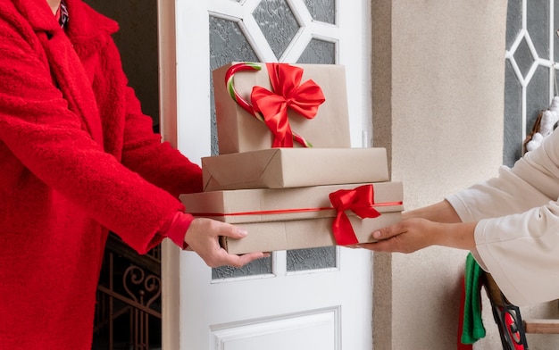 Arbeiter im roten Mantel, der am Vorabend der Feiertage Geschenkboxen in der Nähe der weißen Tür liefert