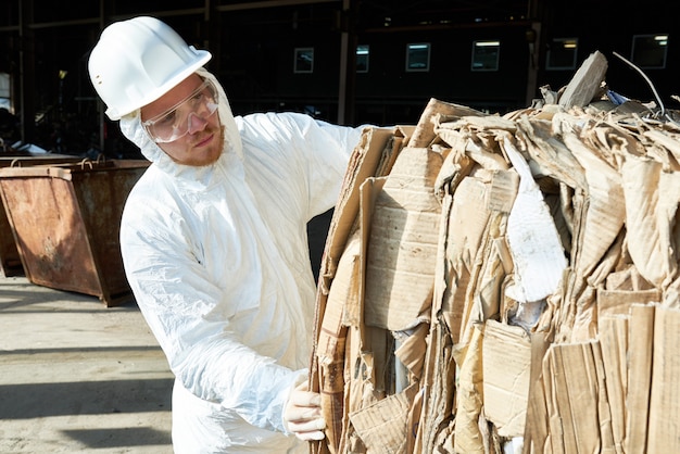 Arbeiter in Hazmat Suit Sorting Cardboard in der Recyclingfabrik