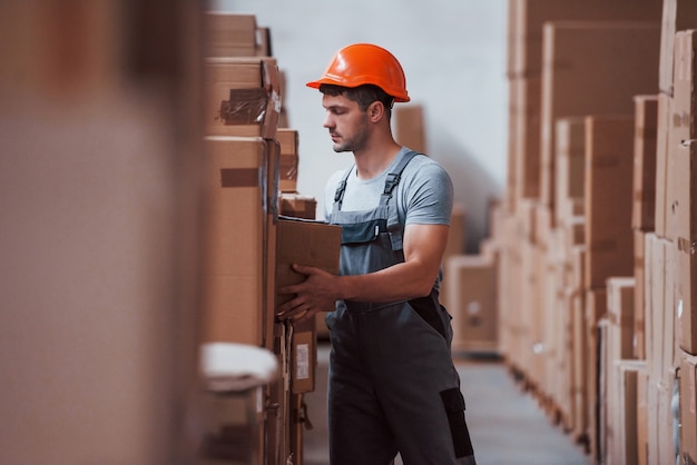 Arbeiter in orangefarbenem Hartmetall ist mit Box in den Händen im Lager.