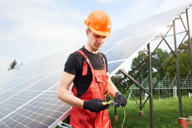 Arbeiter in orangefarbener Uniform mit Ausrüstung zur Hand auf einem Hintergrund von Sonnenkollektoren