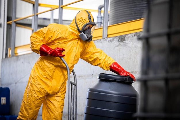 Arbeiter in schützenden Hazmat-Anzug-Gasmaskenhandschuhen, die Fässer mit aggressiven Chemikalien bewegen