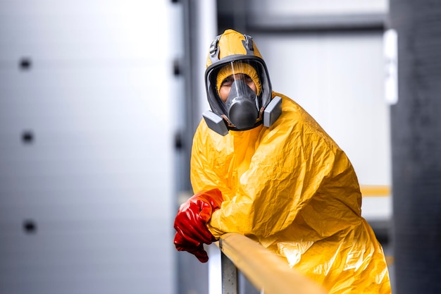 Arbeiter in Schutzanzug, Gasmaske und Handschuhen, die sich im Chemiewerk an den Zaun lehnen