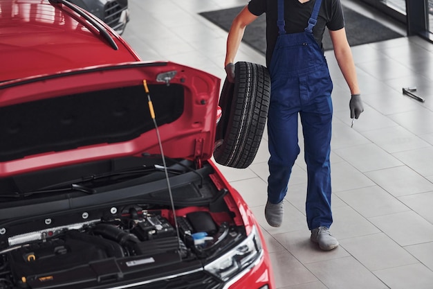 Arbeiter in schwarz-blauer Uniform hält Autorad und geht mit in nahe rotem Auto