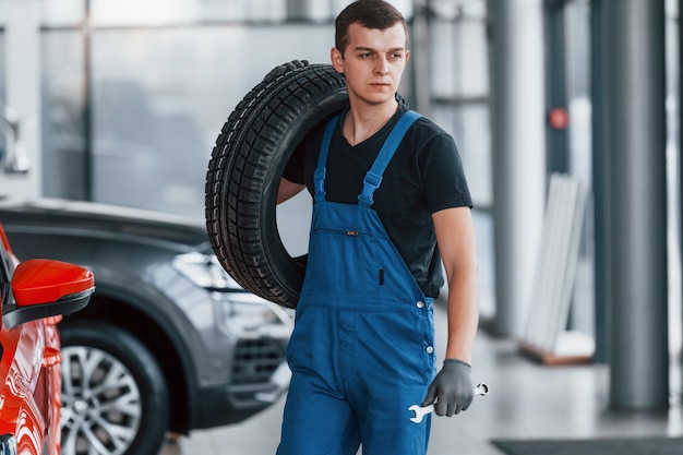 Arbeiter in schwarzer und blauer Uniform, die Autorad halten und Arbeit drinnen haben