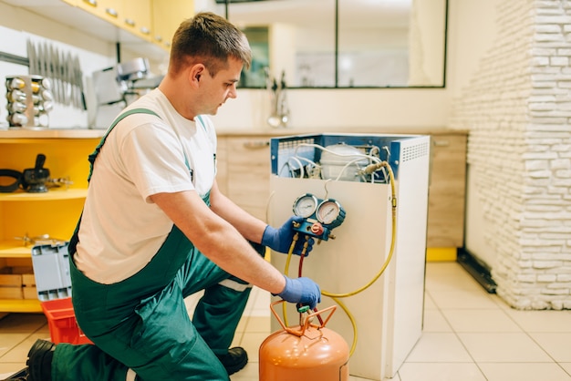 Arbeiter in Uniform füllt Kompressor des Kühlschranks