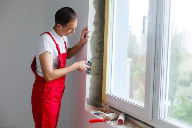 arbeiter in uniform installiert eine kunststoff-sandwichplatte an den schrägen des fensters