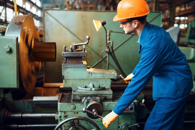 Arbeiter in Uniform und Helm arbeitet an Drehbank, Fabrik. Industrielle Fertigung, Schlossereitechnik, Kraftmaschinenbau