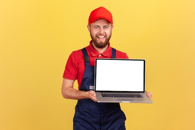 Arbeiter Mann steht und zeigt Laptop mit leerem Bildschirm für Werbung, der lächelnd in die Kamera schaut