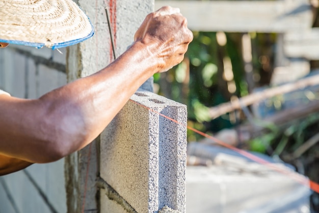 Arbeiter Mauerwerk bauen Wände mit Zementblöcken und Mörtel, indem sie in Schichten aufbauen.