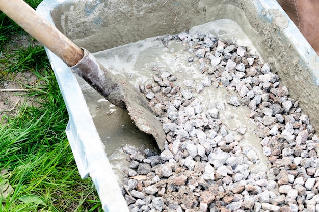 Arbeiter mischen, rühren Zementschlamm, Betonschuttmörtel mit Schaufel in großer Schüssel, Reservoir, Trog, Eimer. Vorbereitung für den Bauprozess, Renovierung, Fundament legen.