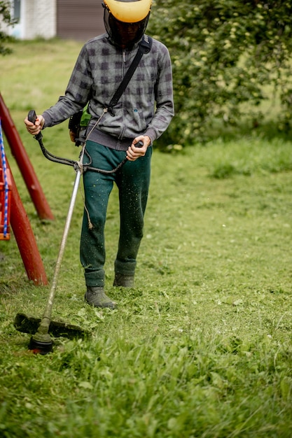 Arbeiter mit einem Gasmäher in der Hand, der vor dem Haus Gras mäht