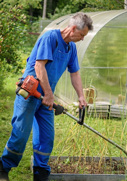 Arbeiter mit einem Handtrimmer in seinen Händen mäht das Gras vor dem Haus Der Trimmer ist in den Händen eines Mannes Der Gärtner schneidet das Gras Lifestyle