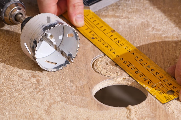 Arbeiter mit Fräser in Aktion beim Werkstatttischler, der Löcher in die Holzplatte macht