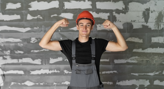 Arbeiter mit orangefarbenem Helmhelm in der Nähe einer Steinmauer. hebt die Hände hoch zeigt Stärke