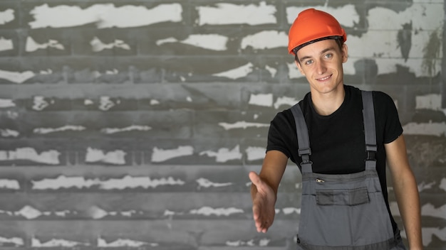 Arbeiter mit orangefarbenem Helmhelm in der Nähe einer Steinmauer. Streckt die Hand zum Händedruck aus.