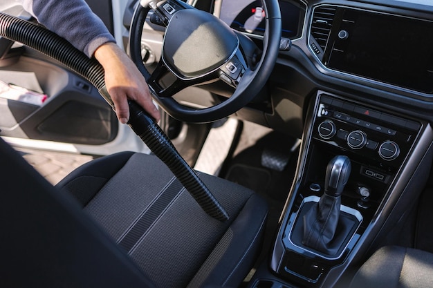 Arbeiter saugen Auto beim Selbstbedienungs-Autowaschmann mit Staubsauger, um Staub zu entfernen und