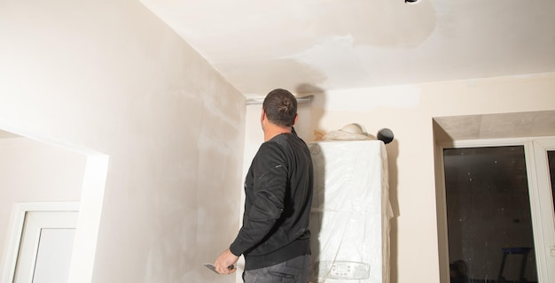 Arbeiter trägt Spachtelmasse an einer Wand auf Haus renovieren