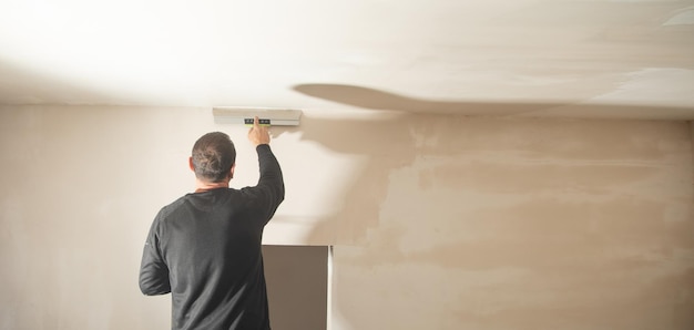 Arbeiter trägt Spachtelmasse an einer Wand auf Haus renovieren