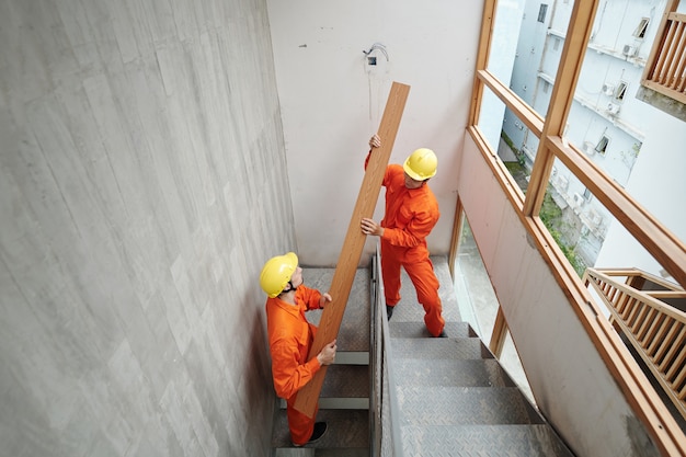 Arbeiter tragen langes Brett die schmale Treppe des im Bau befindlichen Hauses hinauf