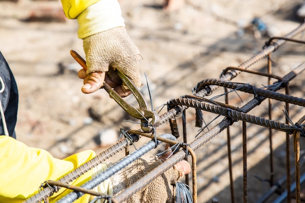 Arbeiter verwenden Draht und Zangen, um den Bewehrungsstab zu binden, der für den Bau von Fundamenten verwendet wird.