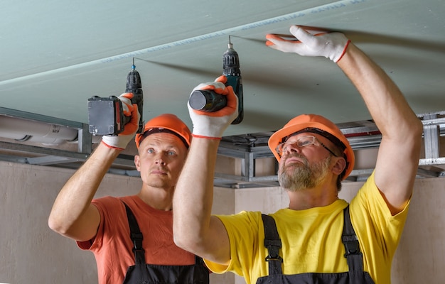 Arbeiter verwenden Schraubendreher, um Gipskartonplatten an der Decke zu befestigen