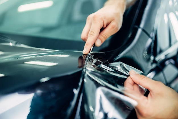 Arbeiterhände bringt Autolackschutzfolie auf der Motorhaube an. Transparente Schutzbeschichtung gegen Späne und Kratzer