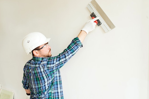 Arbeiterhand mit Spatel auf weißer Wand