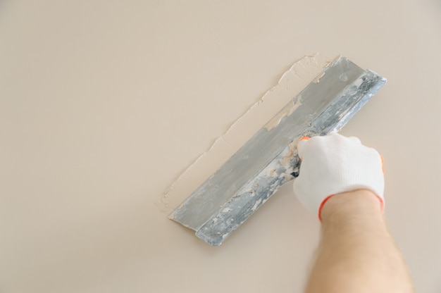 Arbeiterhand verputzt eine Wand mit einem langen Spatel