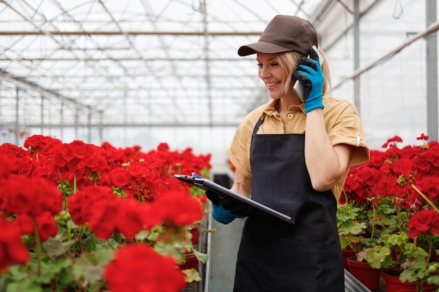 Arbeiterin eines Gewächshauses mit Blumen nimmt telefonisch eine Bestellung von einem Kunden entgegen