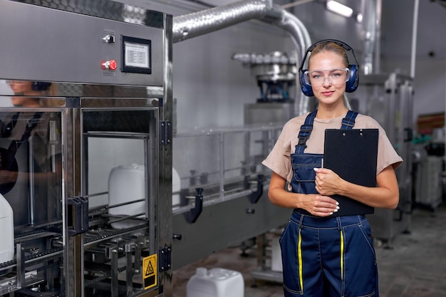 Arbeiterin in Arbeitsschutzkleidung mit Ordner-Tablette, die in der Fabrik arbeitet