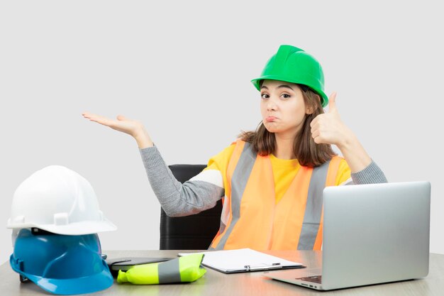 Arbeiterin in Uniform mit geöffneter Handfläche und Daumen nach oben. Foto in hoher Qualität