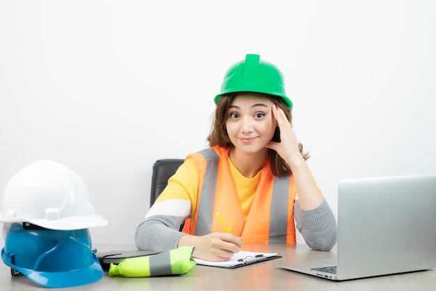 Arbeiterin in Uniform sitzt mit Laptop und Klemmbrett am Schreibtisch. Foto in hoher Qualität