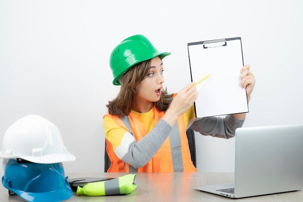 Arbeiterin in Uniform sitzt mit Laptop und Klemmbrett am Schreibtisch. Foto in hoher Qualität