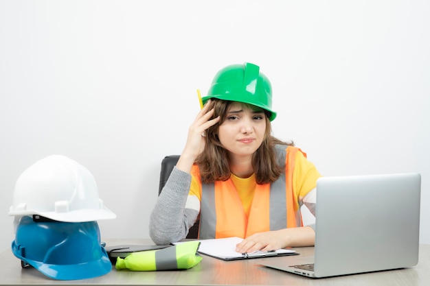 Arbeiterin in Uniform sitzt mit Laptop und Klemmbrett am Schreibtisch. Foto in hoher Qualität