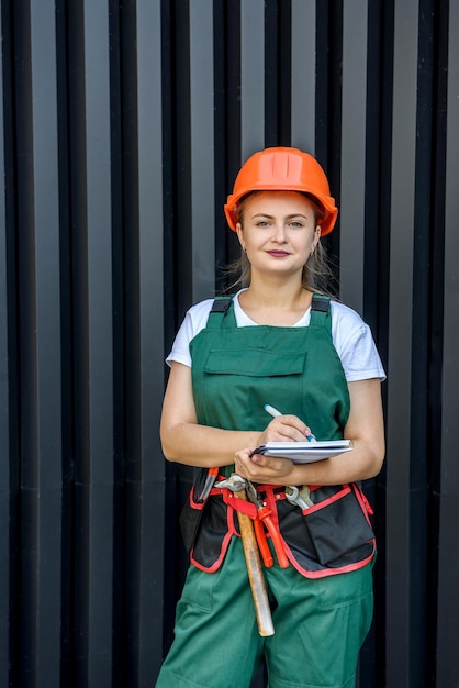 Arbeiterin oder Erbauer. Schöne Dame im Overall und Helm posiert vor dunklem Hintergrund