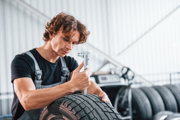 Arbeitet mit Reifen Erwachsener Mann in grauer Uniform ist im Autosalon